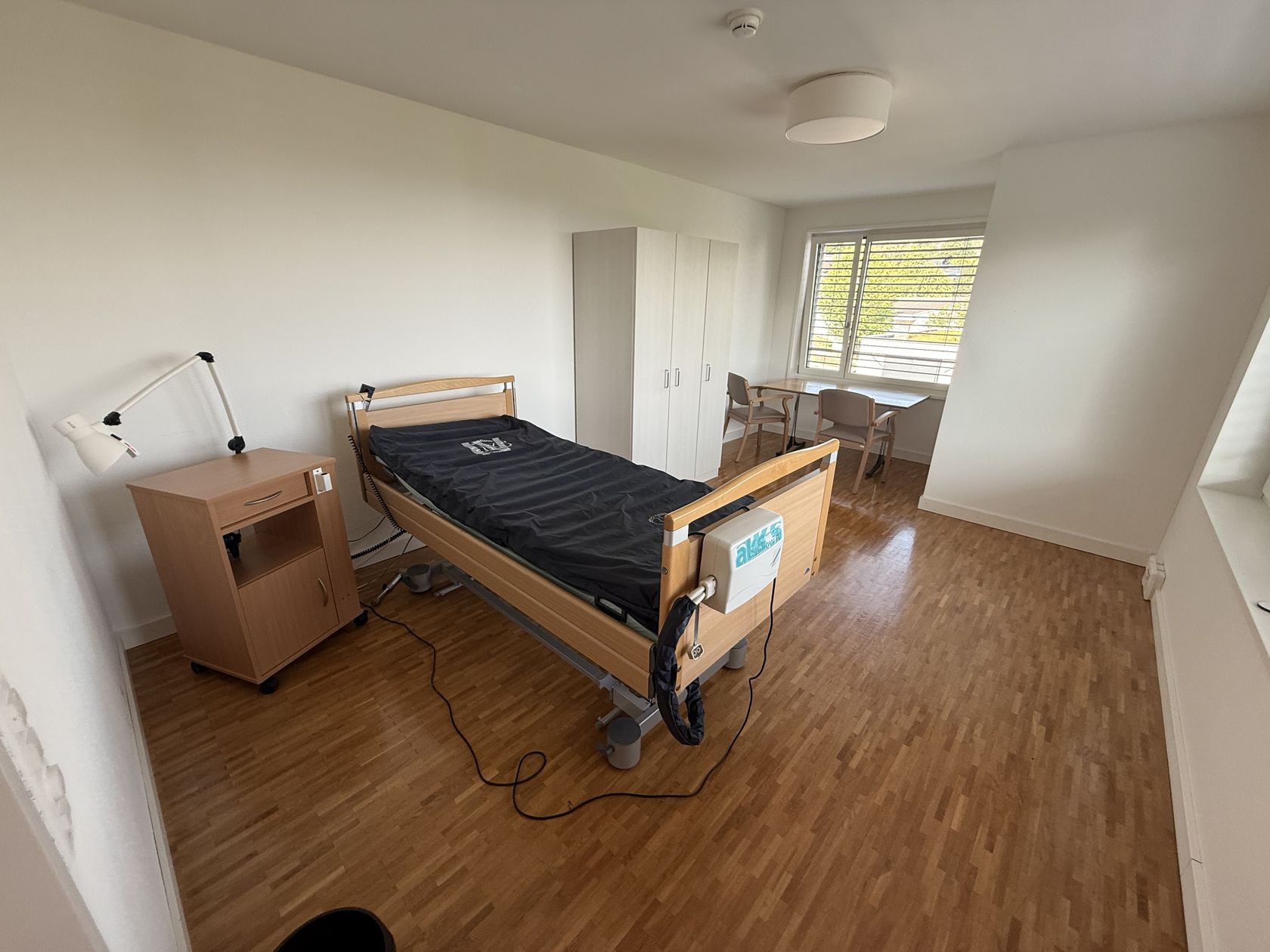 Zimmer mit Pflegebett, Schrank und Sitzecke